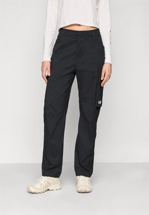 Pantaloni cargo neri realizzati in tessuto resistente, con tasche laterali, chiusura a bottone e una patch con logo sulla coscia. Indossati con sneakers di colore chiaro.