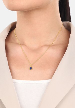 Collar de cadena de oro con un colgante de gema azul ovalada. La cadena es fina y delicada, complementando el vibrante color del colgante.