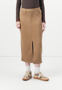 Brauner Wildleder-Midirock mit vorderem Schlitz, ausgestattet mit Kontrastnähten und einem Fünf-Taschen-Design. Kombiniert mit Sneakers im Animal-Print und weißen Socken.
