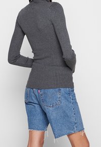 Harmaa ribbineulottu poolokauluksellinen pitkähihainen paita yhdistetty sinisiin farkkushortseihin, joissa on rispaantuneet reunat ja selkäpuolen taskut, joissa on ompeludetailit.