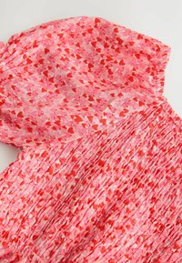 Rosenrotes Kleid mit rotem und hellrosatem Herzmuster, mit gestricktem Oberteil und kurzen Puffärmeln, aus leichtem Stoff gefertigt.