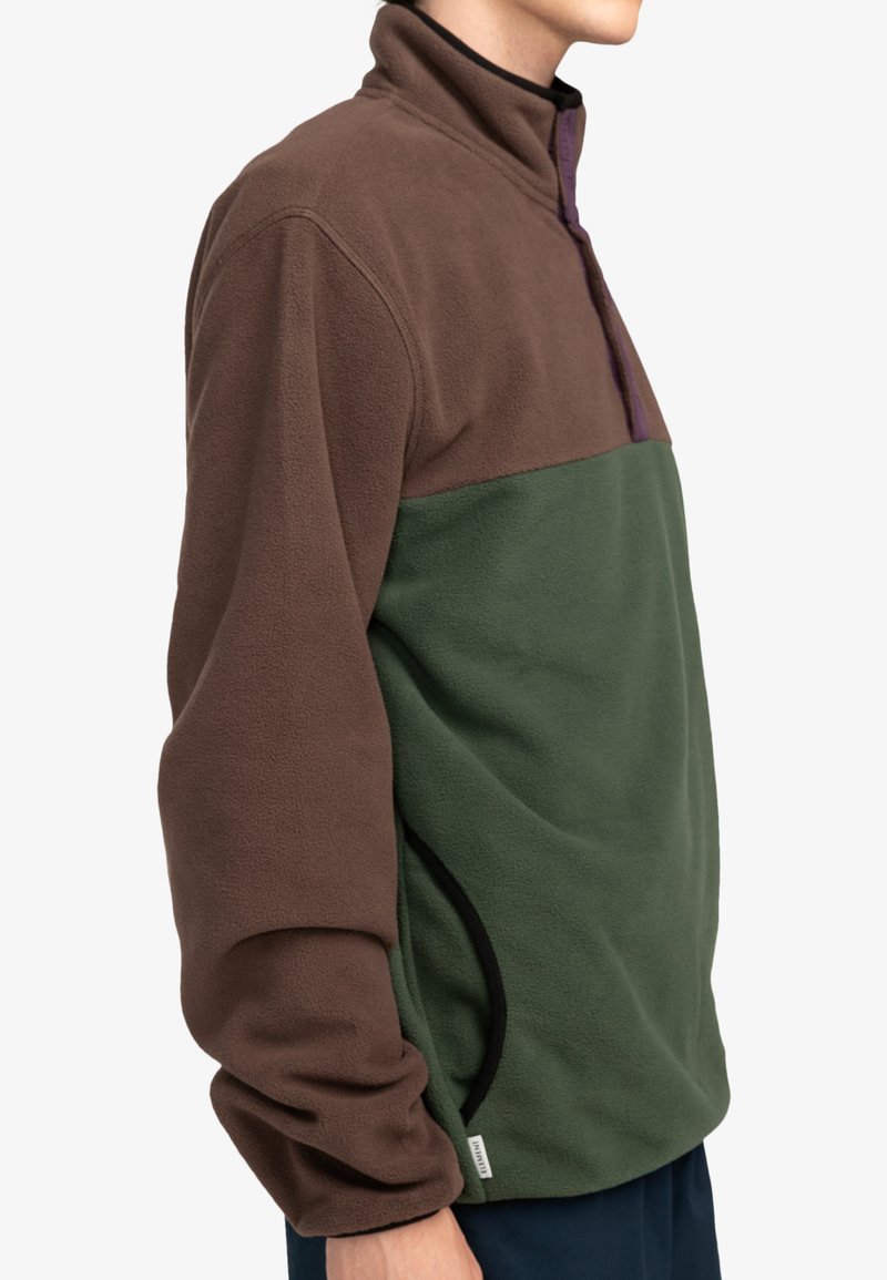 Pullover en polaire de mi-couche avec une partie supérieure marron, une section inférieure verte et des accents violets. Il est doté d'un col haut et de poches latérales.