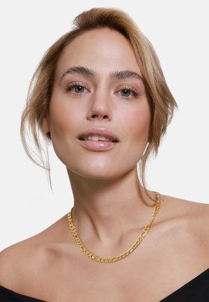 Goldene Halskette mit großen, ineinandergreifenden Gliedern, die eine glatte Textur und einen polierten Glanz aufweisen, direkt auf nackter Haut getragen.