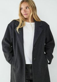 Darker grauer Wollmantel mit klassischem Revers, einreihigem Design und zwei Knöpfen. Verfügt über Seitenﬂecken und eine lockere Passform.