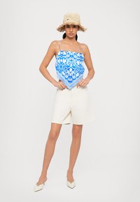 Blue patterned halter top with white shorts, flat white shoes, and a straw hat with fringe. The top features a diamond shape and intricate design.