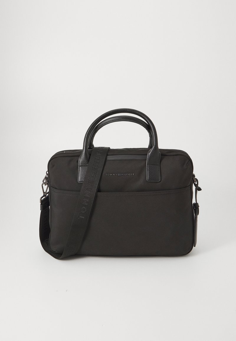 Malette noire en nylon avec des accents en cuir synthétique, deux poignées supérieures et une bandoulière détachable. Présente un logo sur l'avant et une fermeture éclair.