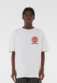 Valge ülemõ�õdus T-särk lühikeste varrukatega, millel on rinnapiiril punane graafiline logo. Puuvillane materjal ja mugav lõige.