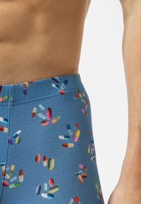 Pantalons en tissu bleu avec un motif coloré de pilules, comprenant diverses formes et tailles de capsules et de comprimés à travers le design.