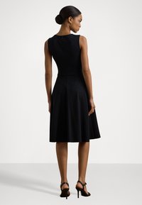 Melna bez piedurknēm kleita ar pieguļošu topu un izplestu svārku, ar augstu kakla izgriezumu un slēptu aizmugurējo rāvējslēdzēju. Melnas augstpapēžu čības.