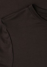 Gros plan sur un tissu en coton brun foncé montrant la couture d'épaule cousue et l'encolure ronde d'un t-shirt uni.