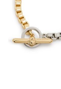 Collana a doppia catena in oro e argento con anello circolare e chiusura decorativa con logo inciso. I collegamenti texturizzati arricchiscono il design.