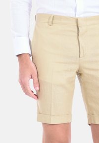 Pantaloni corti in lino beige con una vestibilità su misura, orlo risvoltato e tasche laterali. Il materiale presenta una texture sottile; chiusura con zip e passanti per la cintura inclusi.