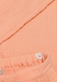 Peske-farvet let stof med en tekstureret finish, der har en samlet talje og en klar knapdetalje.