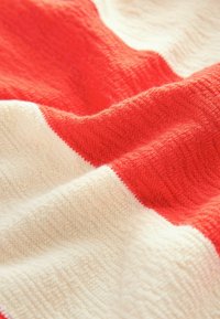 Tissu tricoté doux avec des larges rayures horizontales alternées en rouge et blanc cassé.
