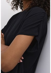 Top noir à coupe ample en tissu texturé. Manches courtes et col rond. Des détails subtils sur le tissu améliorent l'intérêt visuel.