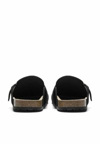 Svart mocka backless tofflor med texturerad korksula, platt gummisul och dekorativ rosett på varje sida.