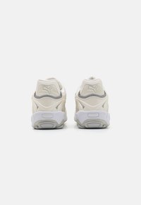Cremefarvede sneakers med et struktureret design og polstret krave. Har en hvid sål med grå accenter og et reflekterende logo på hælen.