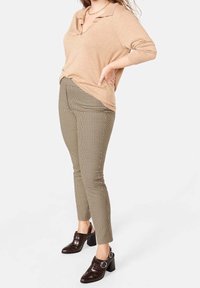 Pullover beige a maglia con colletto, abbinato a pantaloni a sigaretta marrone a motivo houndstooth e mule con tacco marrone scuro dotate di una fibbia circolare.