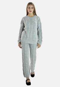 Pull en maille grise et pantalon assorti avec un motif torsadé texturé, présentant une coupe décontractée et des manches longues, associé à des chaussures noires.