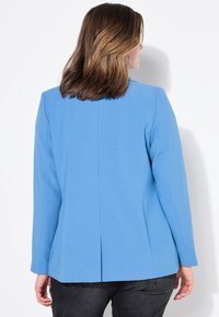 Blazer azul a medida hecho de tela suave. Presenta mangas largas, hombros estructurados y una abertura central en la parte posterior.