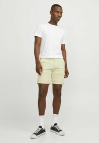 T-shirt blanc à manches courtes associé à un short jaune clair avec un ourlet roulé. Porté avec des baskets noires et des chaussettes blanches montantes.