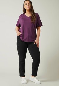 Lila v-ringad t-shirt med avslappnad passform, kombinerad med svarta skinny jeans och vita sneakers. Slät textur, minimalistisk design och avslappnad stil.