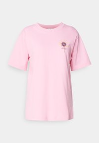 T-shirt en coton rose à manches courtes, avec un motif floral en noir, jaune et marron sur la partie gauche de la poitrine.