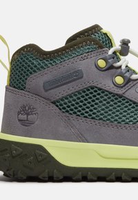 Graue Wildlederschuh für Wanderungen mit Mesh-Einsätzen in Grün, limonengrünen Akzenten, strapazierfähiger Gummisohle mit strukturiertem Grip und Timberland-Logo.