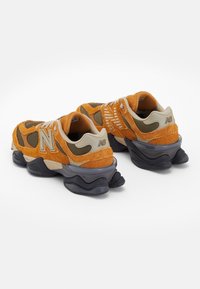 Orange and gray sneakers with a mesh and suede upper, featuring a distinctive wavy sole and prominent logo. Textured accents present.