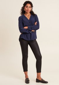Blusa a maniche lunghe blu navy con scollatura a V, due tasche frontali e dettagli con bottoni, abbinata a legging in pelle nera e mocassini neri.