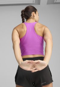 Haut de sport ajusté sans manches de couleur rose vif, associé à un short noir. Le tissu semble lisse avec des détails de couture subtils.