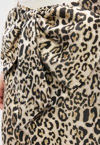 Auduma ar leoparda rakstu brūnās un melnās plankumos; viduklī izšūts izteiksmīgs loks; teksturēts, nedaudz spīdīgs izskats.