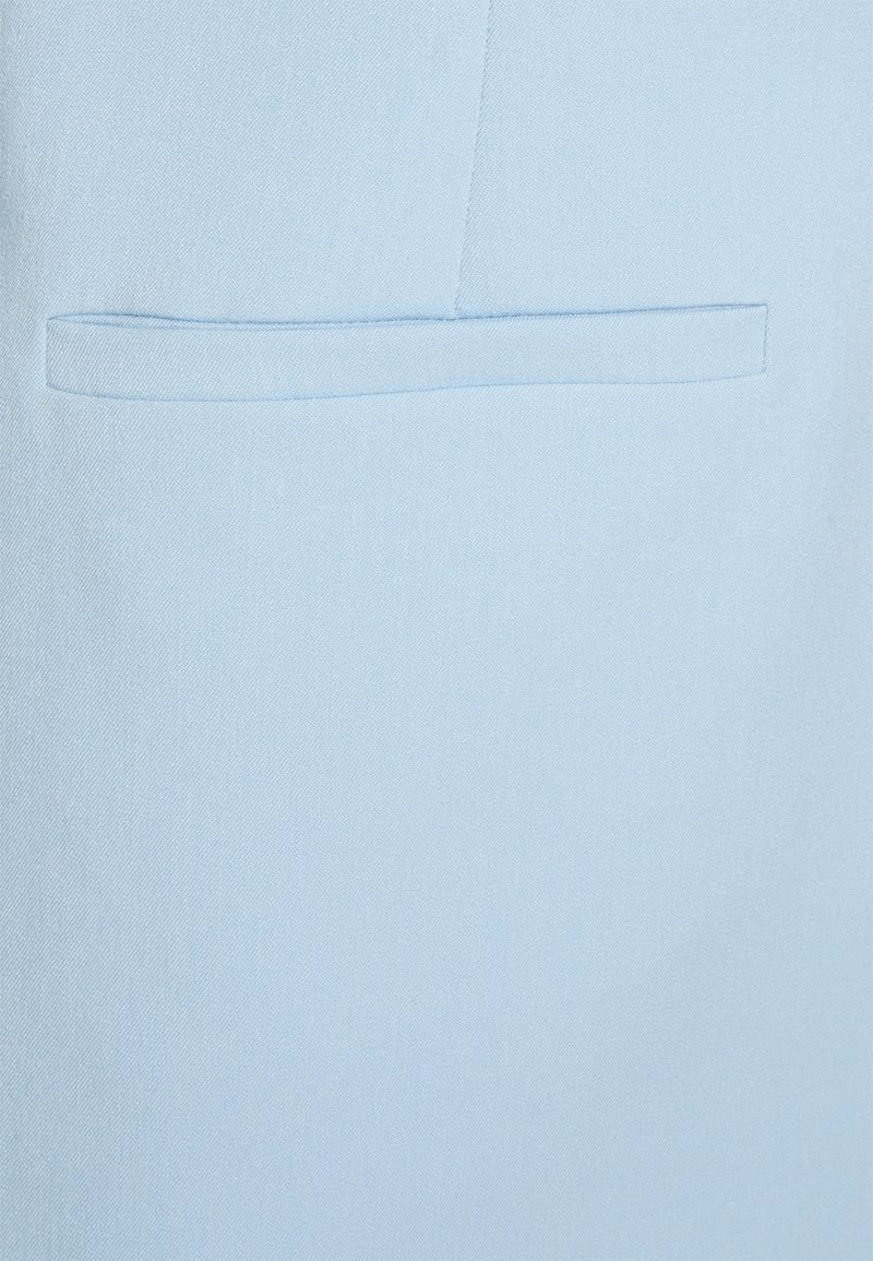Tejido azul claro con una textura suave, que presenta un bolsillo de canto horizontal integrado en el diseño. Construcción simple y limpia.