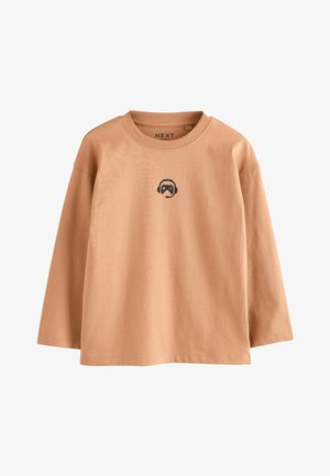 Chemise à manches longues beige clair avec un col rond. Elle présente un petit motif noir d'un casque et d'une manette de jeu sur la poitrine. Matière en coton.