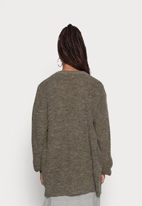 Pletený kardigan v zemitě šedohnědé barvě s volným střihem, kulatým výstřihem a dlouhými rukávy. Má boční rozparky pro větší pohyb a prodyšnost.