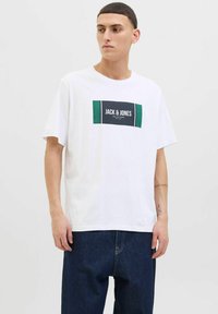 Balta medvilnės marškinėliai su stačiakampiu juodu ir žaliu logotipu, kuriame įrašyta "JACK & JONES", esantis krūtinės centre. Trumpomis rankovėmis, laisvas kirpimas.