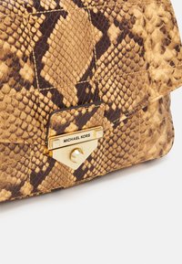 Brązowa i żółta torebka w wzór skóry węża z zapięciem w kolorze złota i grawerem "Michael Kors" na akcentowej blaszce. Teksturowana powierzchnia.