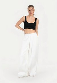 Zwarte cropped top gecombineerd met witte wijde broekspijpen. De stof lijkt glad; de broek heeft voorplooien en een ontspannen pasvorm.