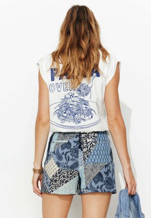 T-shirt sans manches blanc avec un design graphique bleu et un short en patchwork à motifs bleus présentant des motifs floraux et géométriques.