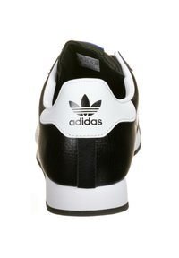 Černobílá teniska Adidas s texturovanou koženou svrchní částí, kulatou patou a výrazným logem na zadní straně. Má polstrovaný límec.