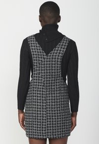 Črna rebrasta turtleneck majica pod črno-belo karirasto obleko z naramnicami po meri in prilegajočo silhueto.