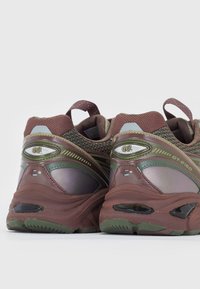 Scarpe da ginnastica marroni e verdi con una parte superiore in rete testurizzata e accenti riflettenti, dotate di un collo imbottito e dettagli con logo sul tallone.
