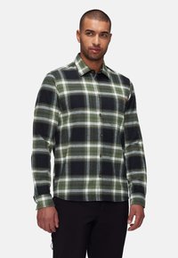 Camicia in flanella a quadri verdi e neri con chiusura a bottoni, colletto e maniche lunghe. Presenta bottoni marroni e un sottile accento del logo.