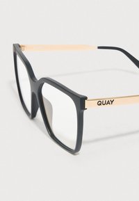 Čierne obdĺžnikové okuliare s matným povrchom, zlatými akcentmi na straniciach a priesvitnými šošovkami. Na jednej stranici je vyrazené slovo "QUAY".