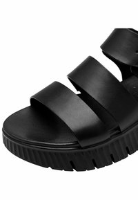 Schwarze Sandalen mit drei breiten Riemen aus Leder, einer strukturierten Innensohle und einer dicken, geriffelten Gummisohle.