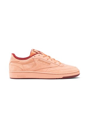 Zapatillas Reebok en ante color salmón, con detalles en rojo en la lengüeta, el collar y la suela; diseño clásico con cordones y superficie texturizada.