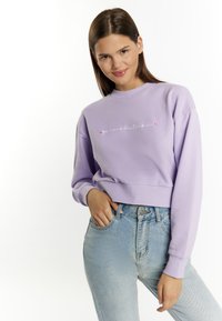 Liliowy sweter z okrągłym dekoltem z ribbed, z haftowanym napisem i akcentami w kształcie serca, w zestawieniu z jasnoniebieskimi spodniami typu high-waisted.