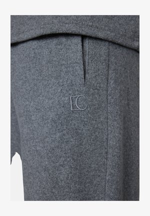 Close-up of gray knit pants with side pocket and small embroidered logo with letter E and C on thigh.