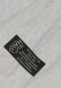 Grått tyg med melerad struktur; har en svart etikett med vit text som visar produktinformation och varumärkesdetaljer.