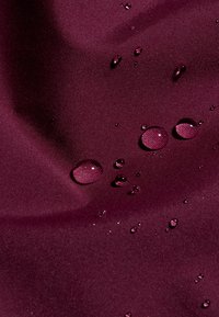 Vinrött tyg med en slät textur, med flera synliga vattendroppar på ytan.